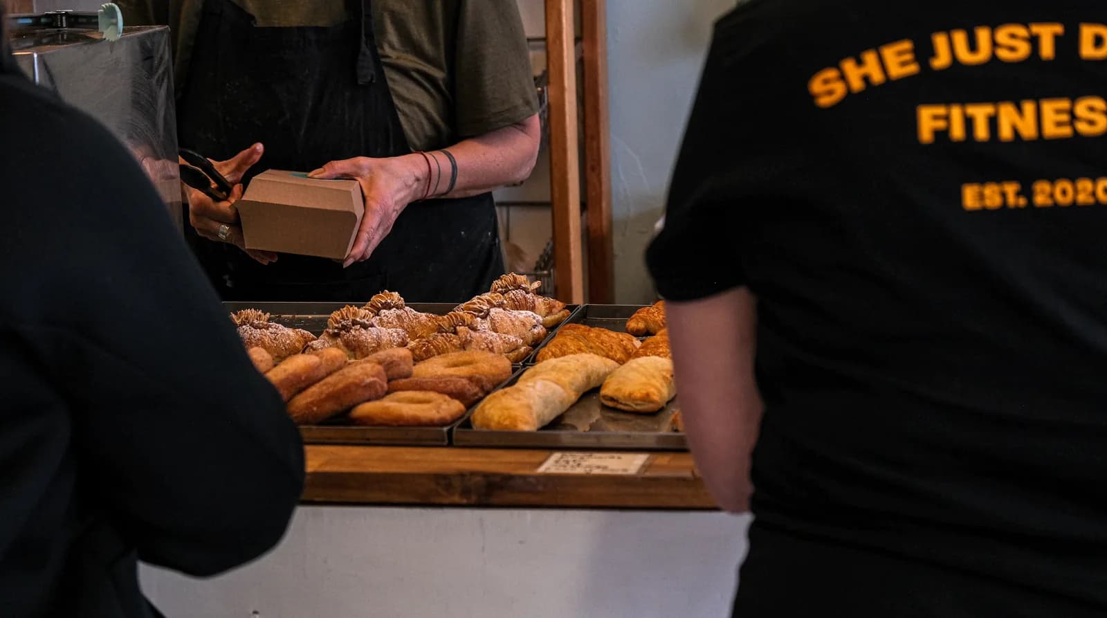 Pastries on a bakery counter with a person holding a takeaway box